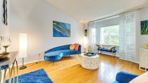 A modern living room with a blue sofa, a round coffee table, and a large window with blinds.