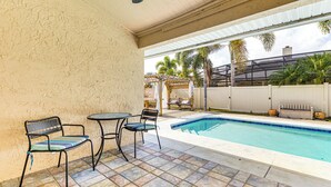 A covered patio with a pool, two chairs, and a table.
