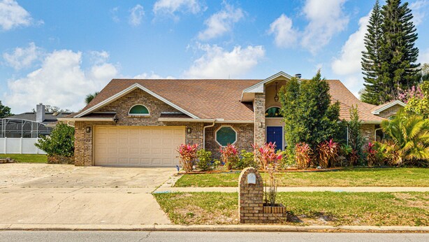 A two-story house with a brick facade, a garage, and a well-maintained front yard with various plants and a mailbox.