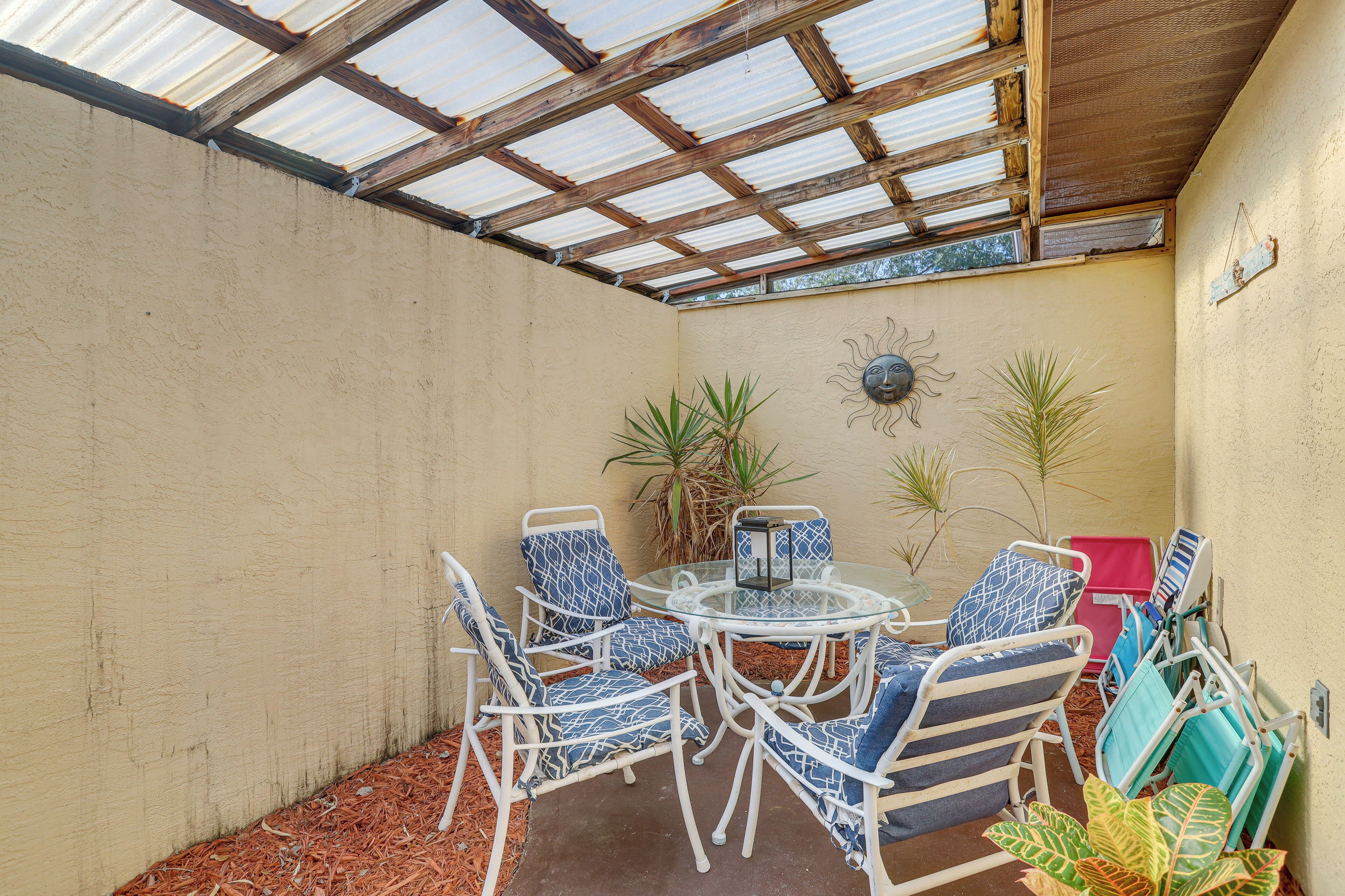 Un patio couvert aménagé avec des meubles en osier blanc, une table en verre et des plantes en pot.