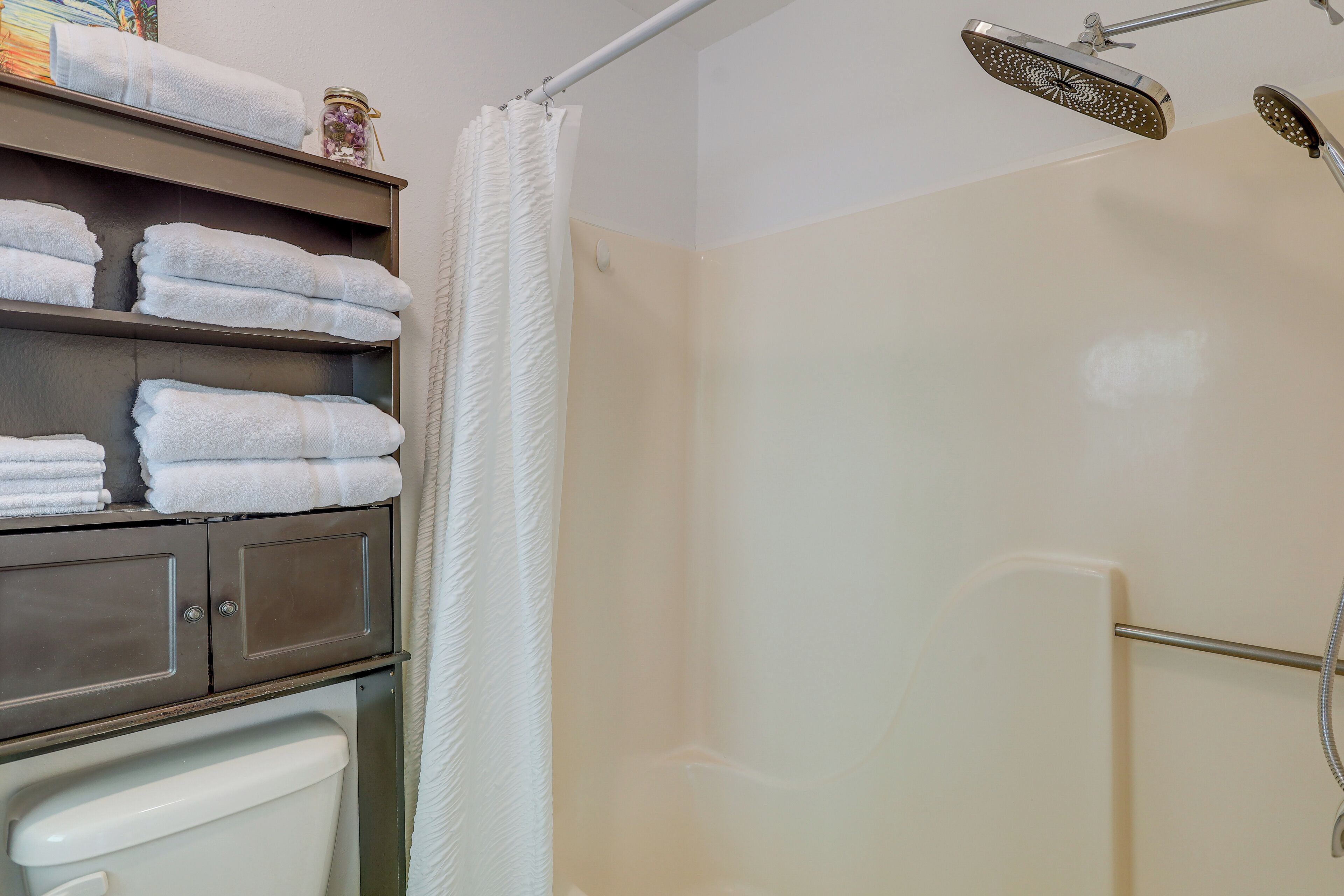 A bathroom with a shower, a toilet, and a shelf with neatly folded towels.
