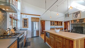 Une cuisine moderne dotée d’un îlot central, d’appareils électroménagers en acier inoxydable, de meubles de rangement en bois et de luminaires suspendus.