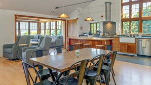 Un vaste espace de vie comprenant un coin repas avec table et chaises, une cuisine dotée d’un grand îlot central et une vue agréable par les fenêtres.