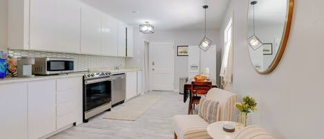 A modern kitchen with white cabinets, a microwave, oven, and a dining area with a sofa and table.