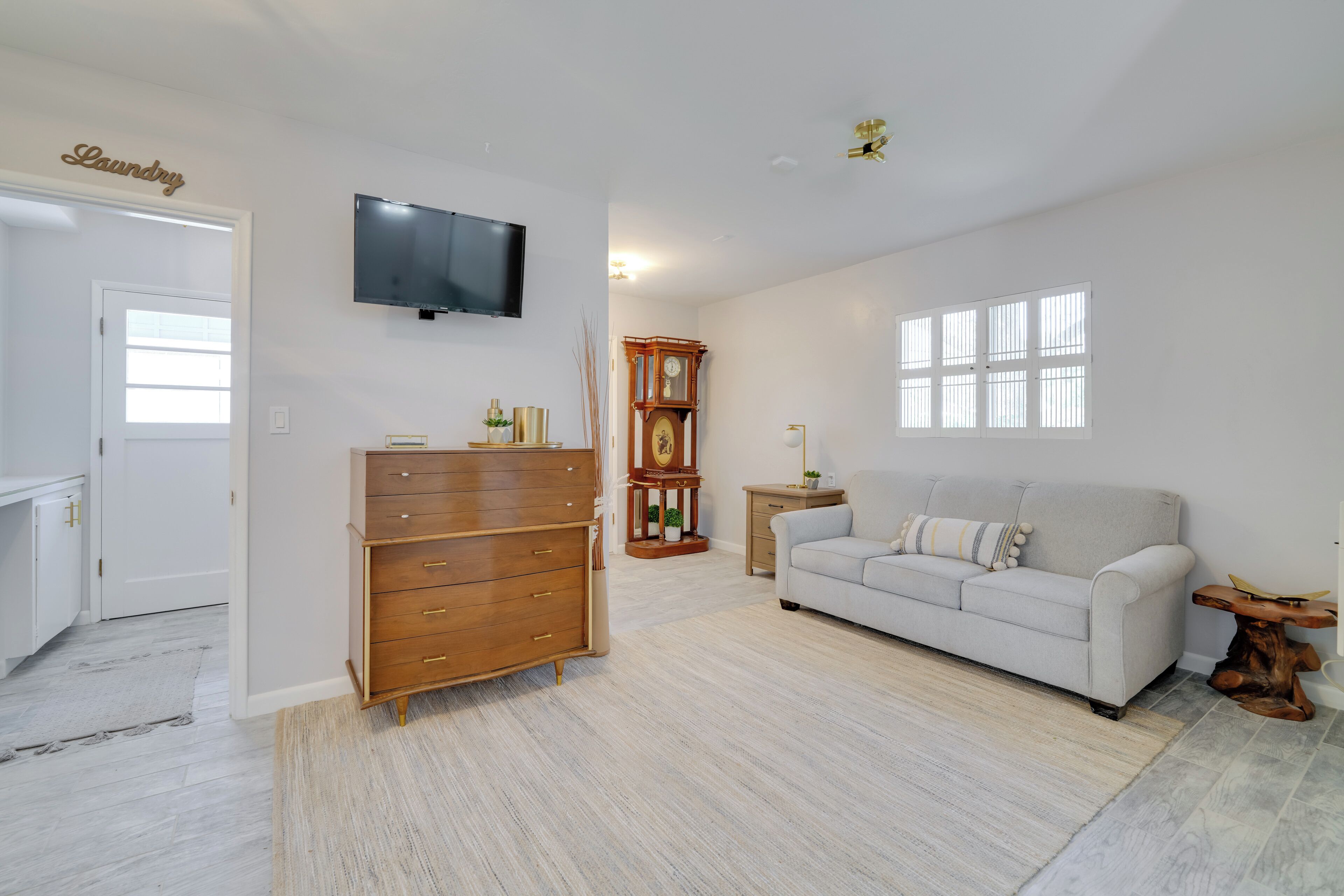 A living room with a white sofa, wooden dresser, and a television on the wall.