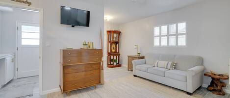 A living room with a white sofa, wooden dresser, and a television on the wall.