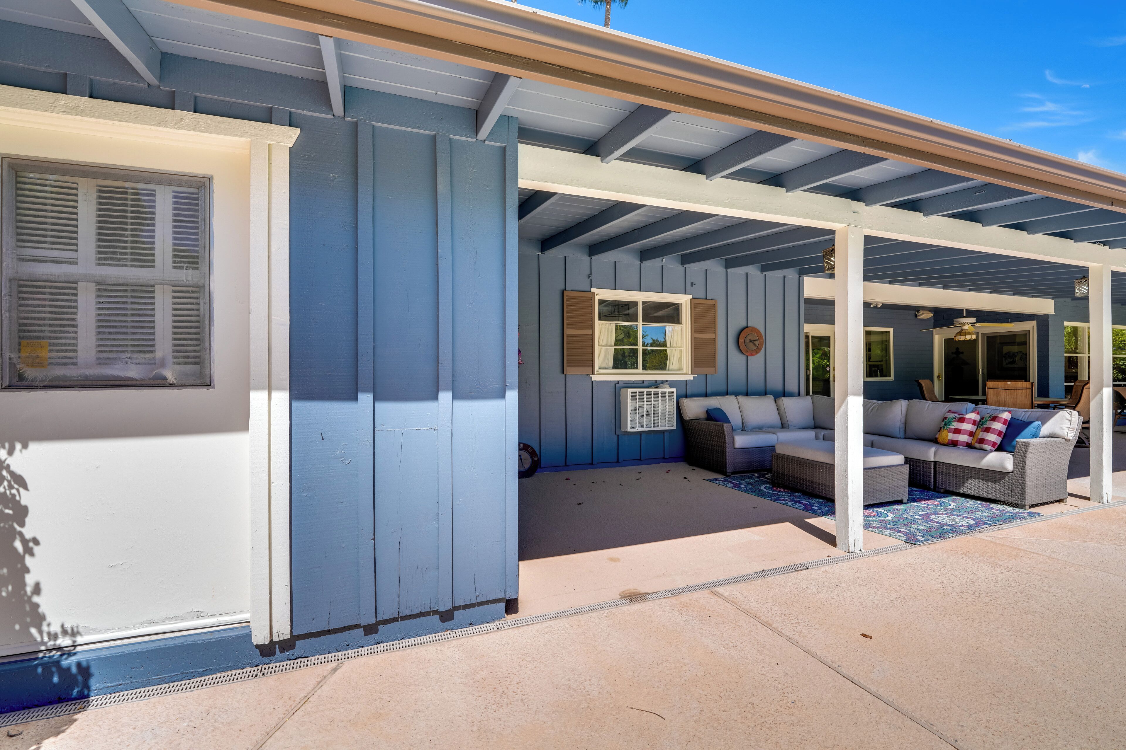 A covered patio area with a white ceiling and blue walls, featuring a sofa set and a small table.