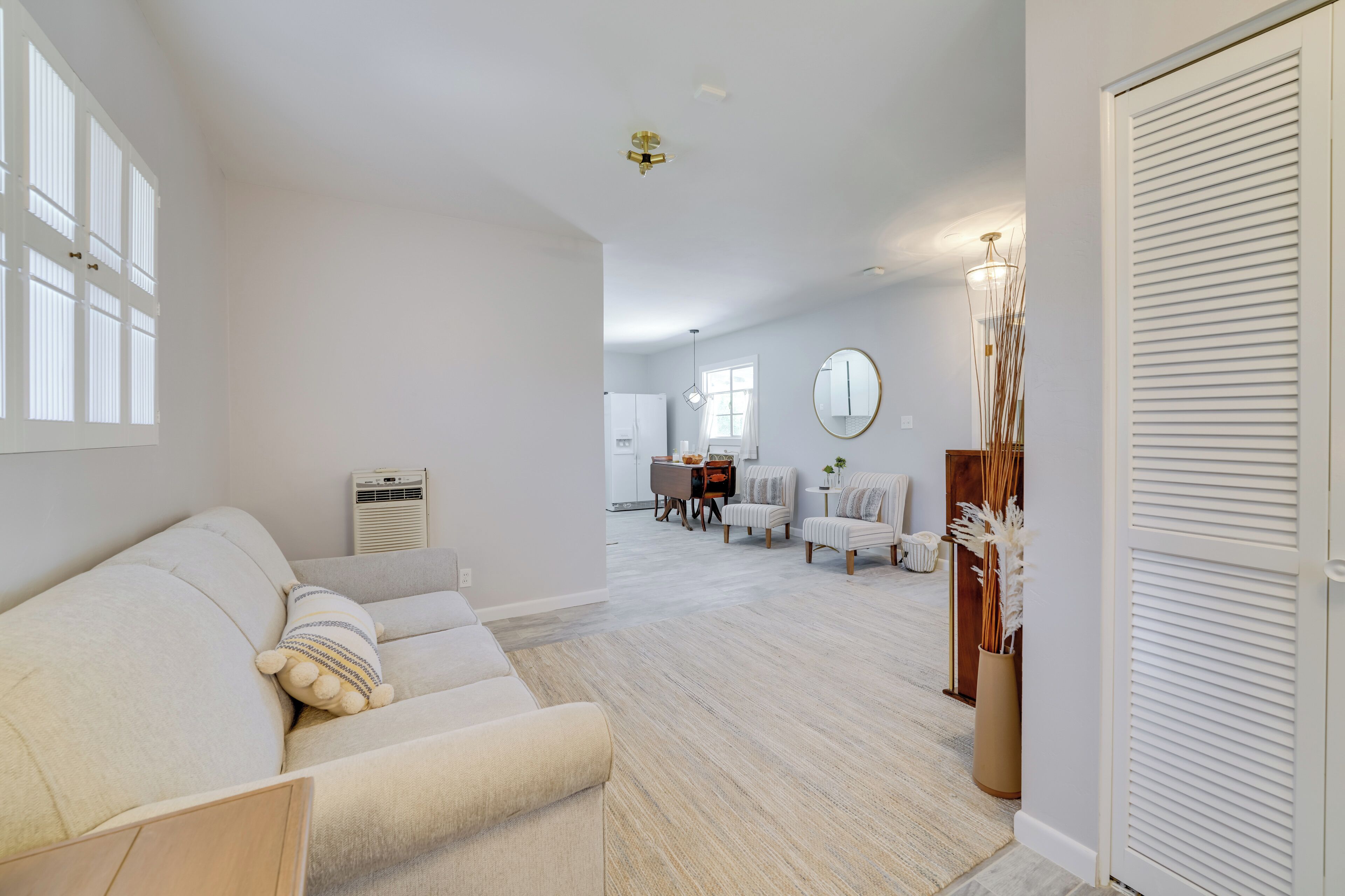 A spacious living room with a sofa, a dining area with chairs, a coffee table, and a kitchen in the background.