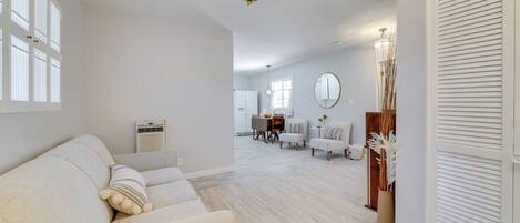 A spacious living room with a sofa, a dining area with chairs, a coffee table, and a kitchen in the background.