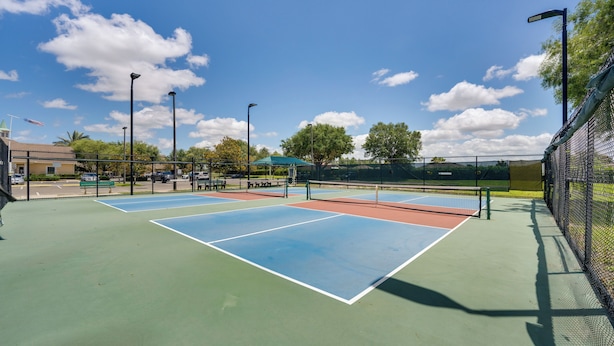Un court de tennis extérieur doté d’une surface de jeu verte et bleue, entouré d’une clôture et éclairé par des lampadaires.