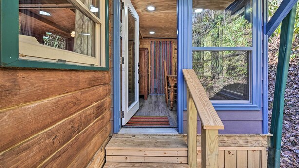 A wooden cabin with a wooden staircase leading to a door, a window on the right, and a wooden railing.