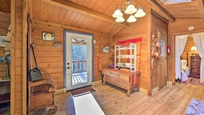 A wooden interior with a door, a bench, a shelf with dishes, and a hanging light fixture.