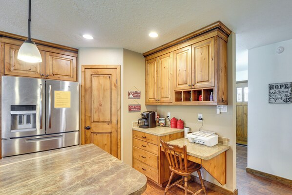 Una cocina con armarios de madera, un refrigerador de acero inoxidable, una mesa de madera y una silla.