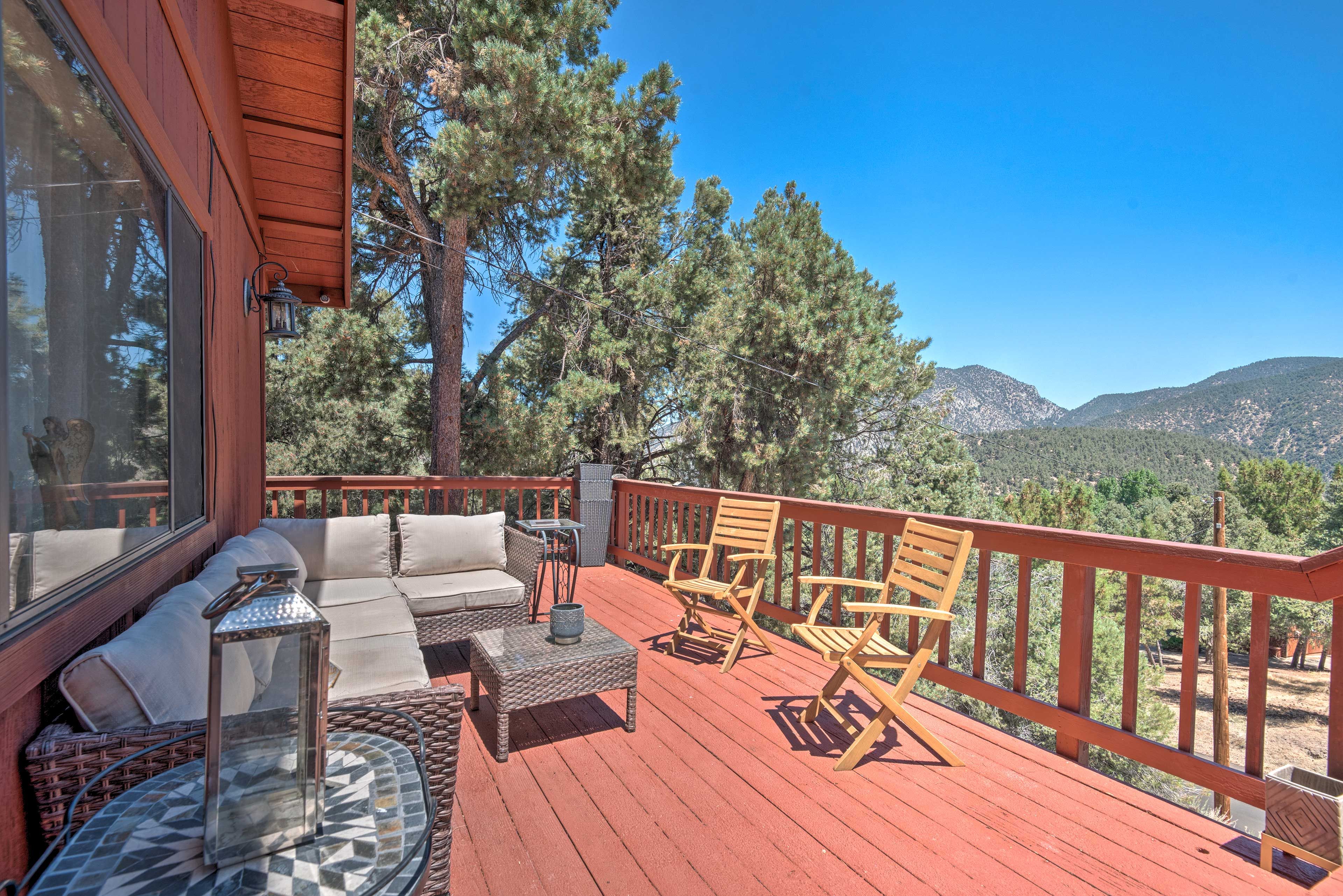 Une terrasse en bois, aménagée avec du mobilier d’extérieur, notamment un canapé et des fauteuils, qui offre une vue sur un paysage montagneux.