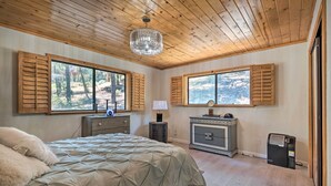 A bedroom with a large bed, wooden shutters on windows, a chandelier, and a heater. - Cozy Pine Mountain Cabin: Hike, Bike, Fish Nearby! (Pine Mountain Club)