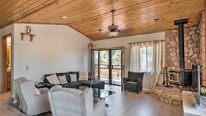 A spacious living room with a stone fireplace, a ceiling fan, and a large window. - Cozy Pine Mountain Cabin: Hike, Bike, Fish Nearby! (Pine Mountain Club)