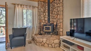 A cozy living room with a stone fireplace, a comfortable armchair, a flat-screen TV, and a stone wall. - Cozy Pine Mountain Cabin: Hike, Bike, Fish Nearby! (Pine Mountain Club)