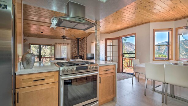 A modern kitchen with a built-in oven, a stove, and a large window overlooking a mountainous landscape. - Cozy Pine Mountain Cabin: Hike, Bike, Fish Nearby! (Pine Mountain Club)