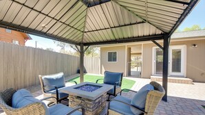 Une terrasse extérieure aménagée avec des meubles en osier, un foyer en pierre et un espace couvert doté d’un toit en métal.