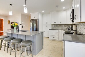 A modern kitchen with white cabinets, a central island with bar stools, stainless steel appliances, and pendant lighting. - Putting Green & Patio: Central Prescott Home (Prescott)