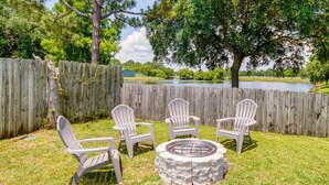 A backyard with a wooden fence, a fire pit, and four Adirondack chairs. - Gulf Breeze Vacation Rental for 2 w/ Pool Access! (Gulf Breeze)