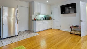 A modern kitchen with white cabinets, a stainless steel refrigerator, a microwave, and a TV mounted on the wall. - Gulf Breeze Vacation Rental for 2 w/ Pool Access! (Gulf Breeze)