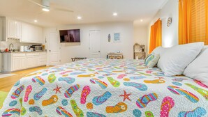 A bedroom with a colorful bedspread, a white ceiling fan, and a view of the kitchen in the background. - Gulf Breeze Vacation Rental for 2 w/ Pool Access! (Gulf Breeze)