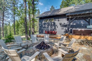 Une cabane en bois avec un foyer entouré de fauteuils Adirondack, une terrasse avec des chaises rouges et un jacuzzi.