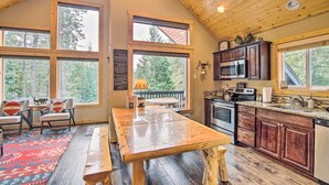 Un'ampia cucina con mobili in legno, una grande isola e vista sulla foresta attraverso ampie finestre.