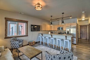 A modern kitchen with bar stools, a dining area with patterned chairs, and a large window. - Montana Vacation Rental - Fish, Hike, Ski! (Columbia Falls)