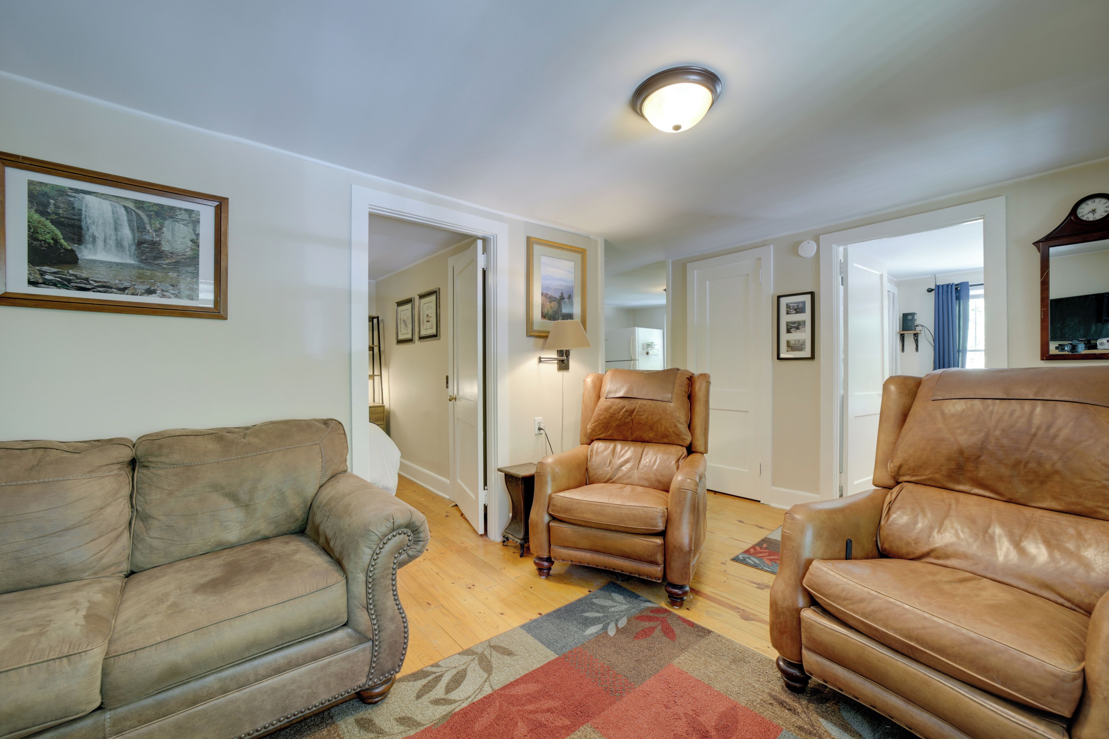 A living room with a brown leather sofa, a brown leather armchair, and a wooden coffee table. There is a framed picture on the wall and a lamp on a side table.
