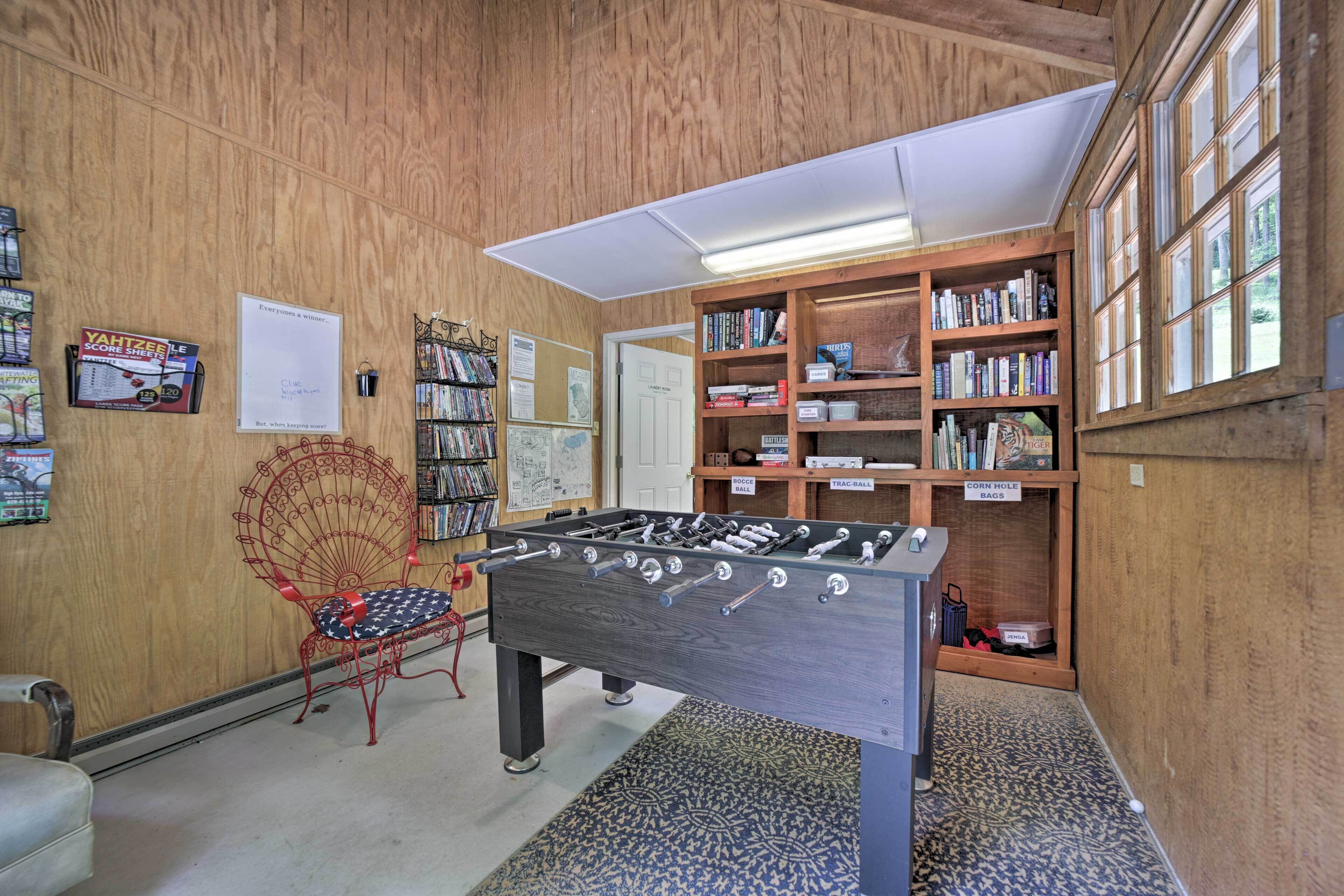A room with a foosball table, a bookshelf, and a window.