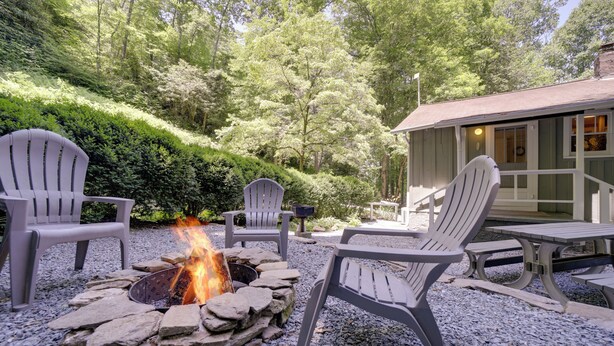 Un foyer est entouré de fauteuils Adirondack et d’une table, le tout installé sur une surface recouverte de gravier, avec un bâtiment visible en arrière-plan.