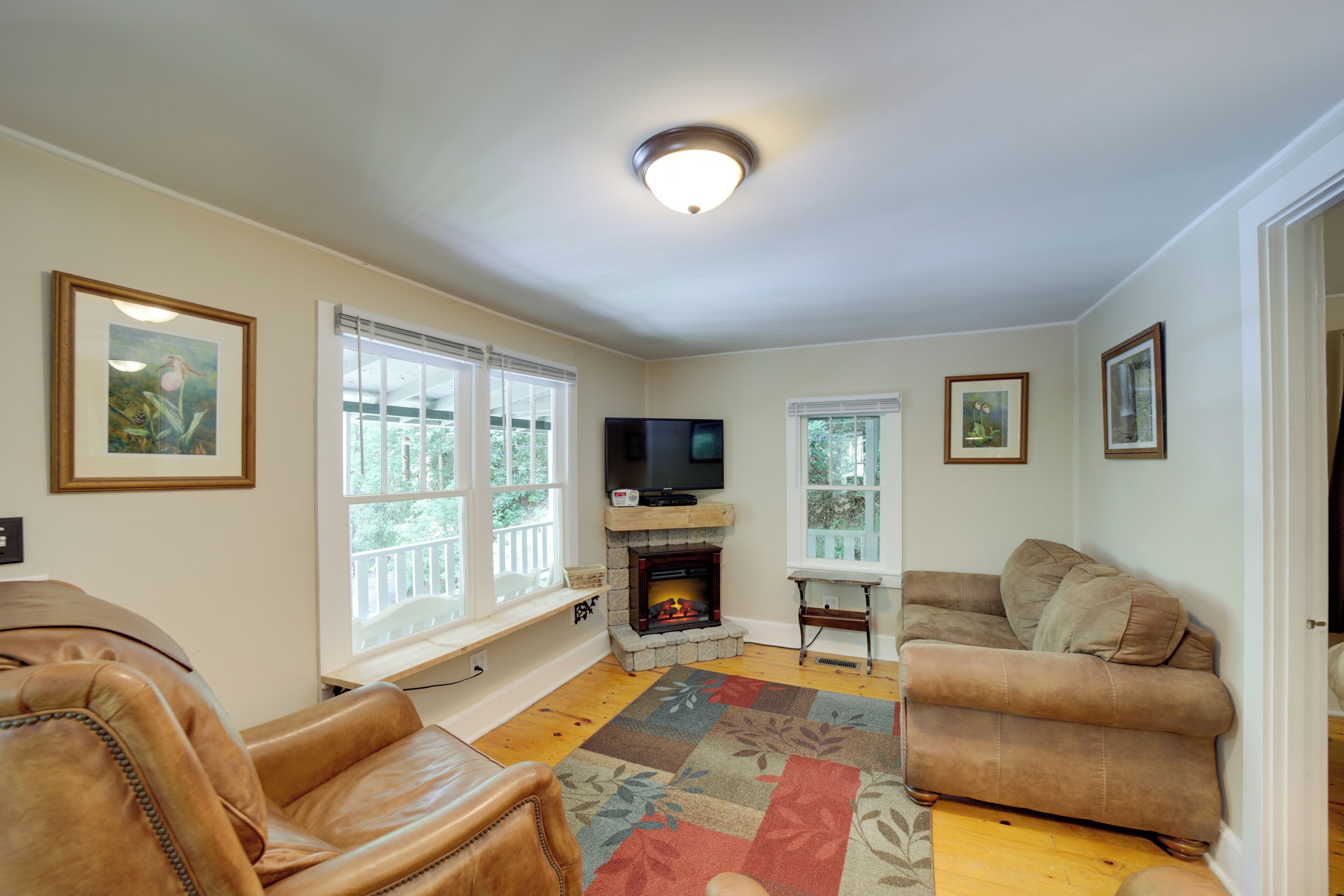 A living room with a fireplace, leather chairs, a television, and framed artwork on the walls.