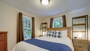 Un lit bien fait, recouvert d’une couverture bleue, avec une tête de lit en bois et deux tables de chevet dotées de lampes.