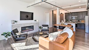 Een moderne woonkamer met een open haard, leren banken en een eethoek, met een keuken op de achtergrond.