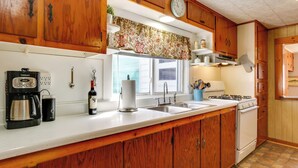 A kitchen with wooden cabinets, a white countertop, a coffee maker, a wine bottle, a paper towel holder, a clock, and a stove. - Scenic Home on the Delaware River, Pet-friendly! (Hancock)
