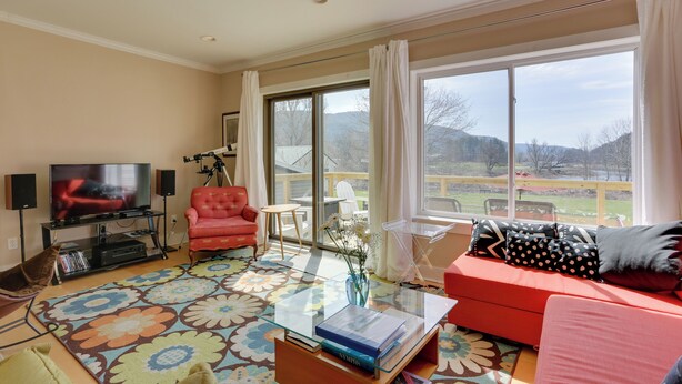 A living room with a TV, red sofa, and a large window with a view of the outdoors. - Scenic Home on the Delaware River, Pet-friendly! (Hancock)
