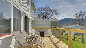 A wooden deck with two lounge chairs and a table, overlooking a grassy yard and a house with a white exterior. - Scenic Home on the Delaware River, Pet-friendly! (Hancock)