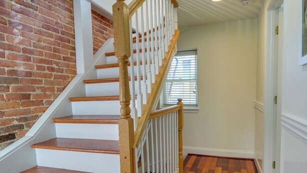 Eine Treppe mit Holzboden und weißen Geländern, die zu einem Raum mit Backsteinwand und Fenster führt.