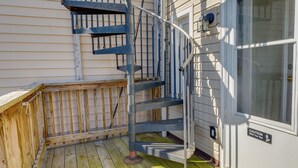 Eine Wendeltreppe führt zu einer Terrasse mit Holzgeländer und einem Warnschild an der Wand.