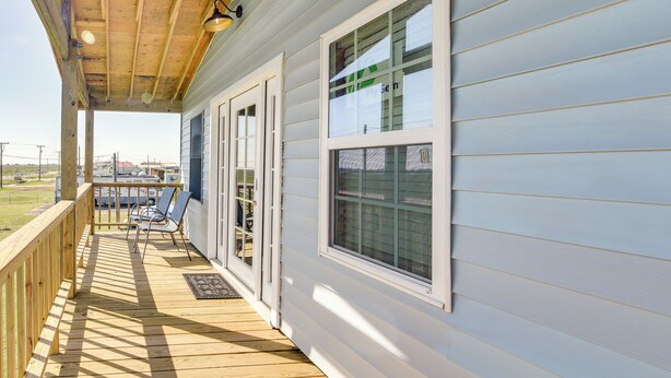 A covered porch with a wooden deck, two sliding glass doors, and a small seating area with chairs. - Waterfront Texas Abode w/ Boat Ramp, Pets Welcome (Bay City)