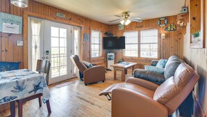 A cozy room with wooden walls, a ceiling fan, a television, a sofa, and a dining table with a starfish tablecloth. - Waterfront Texas Abode w/ Boat Ramp, Pets Welcome (Bay City)