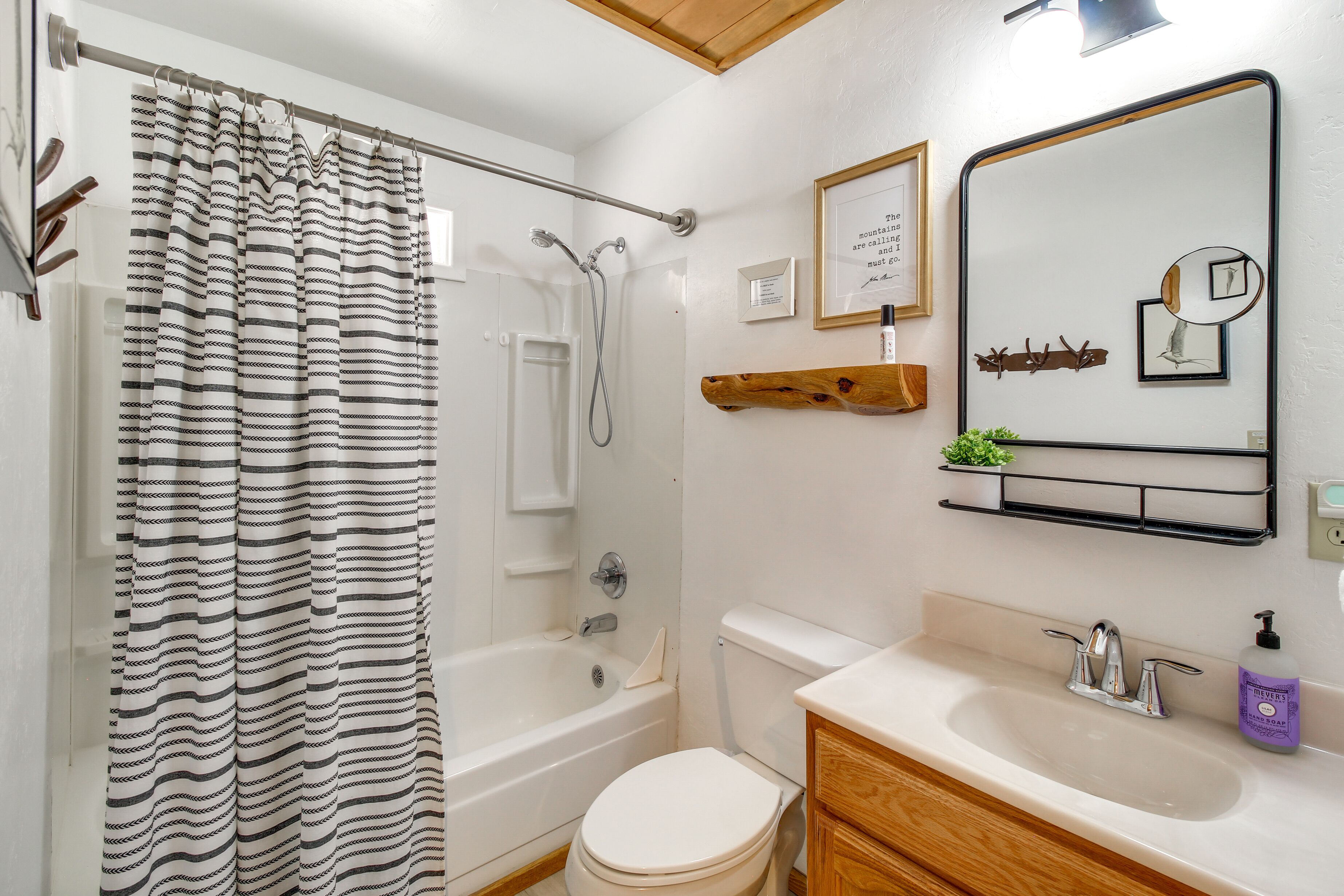 Un baño con cortina de ducha, bañera, inodoro, lavabo y espejo.