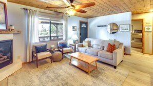 A cozy living room with a fireplace, a sofa, a coffee table, and a ceiling fan. - Cozy Heber Cabin Retreat w/ Deck + Fireplace! (Overgaard)