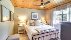 A bedroom with a wooden ceiling, a bed with white bedding, two bedside tables with lamps, and a window with curtains. - Cozy Heber Cabin Retreat w/ Deck + Fireplace! (Overgaard)