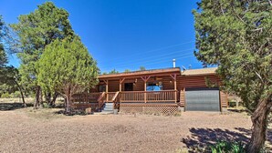 A wooden cabin with a porch, a garage, and a gravel driveway surrounded by trees. - Cozy Heber Cabin Retreat w/ Deck + Fireplace! (Overgaard)