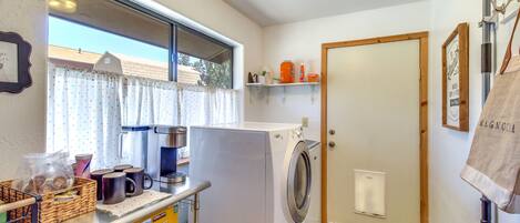 A laundry area with a washing machine, a coffee maker, and a basket of laundry supplies.