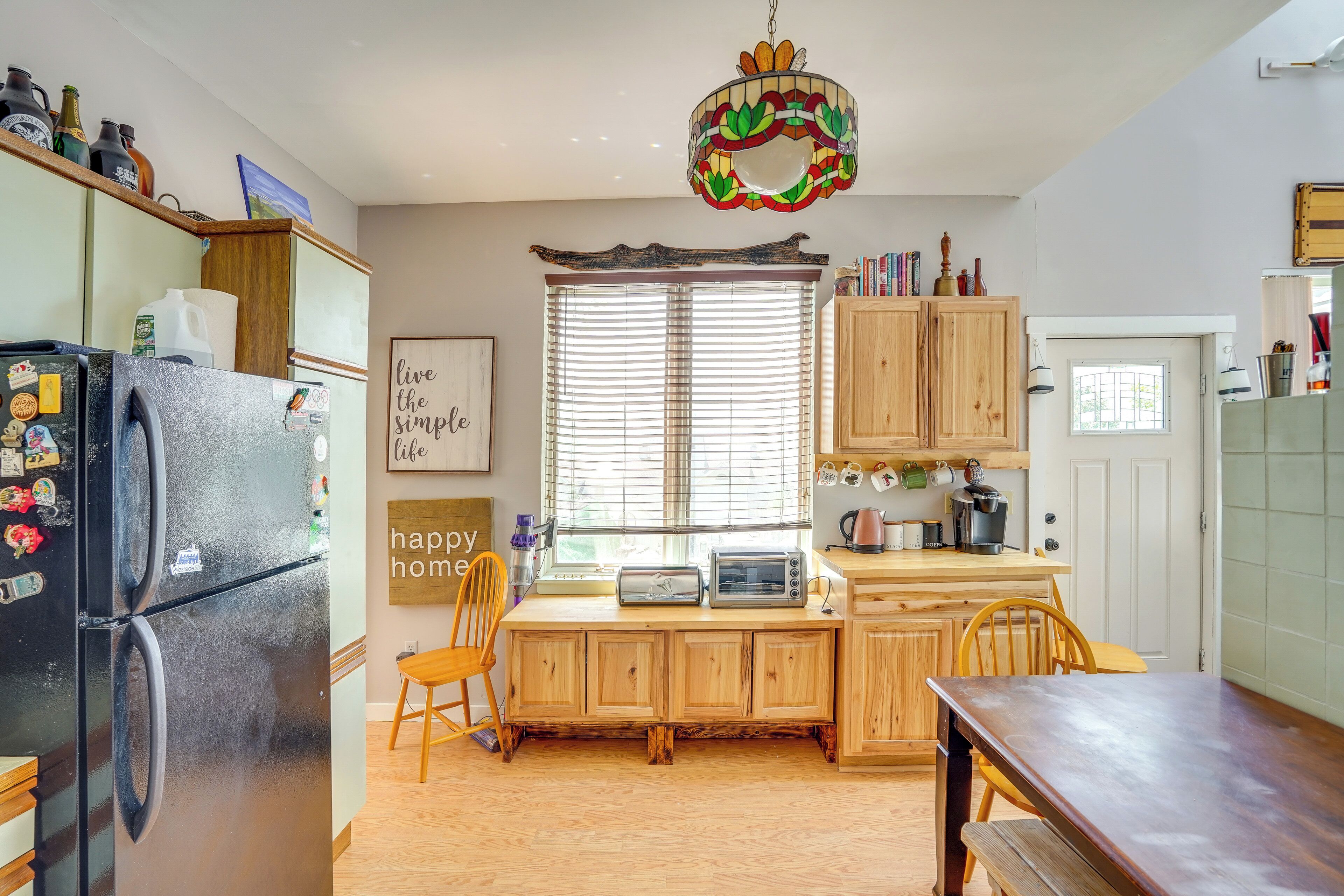 A kitchen with wooden cabinets, a black refrigerator, a wooden dining table, and a window with blinds.