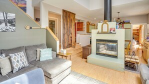 Ein Wohnzimmer mit grauem Sofa, Kamin und einer Treppe, die in einen anderen Raum führt.